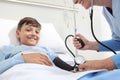 Happy child lying in bed in hospital room and nurse measuring his pressure with sphygmomanometer and stethoscope Royalty Free Stock Photo